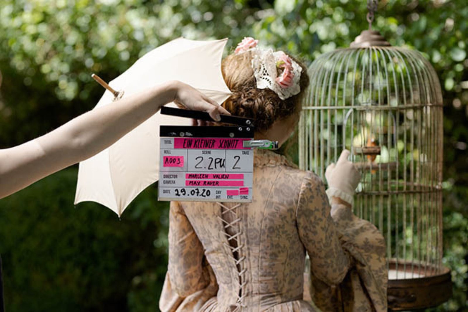 Hand holding film slate in front of woman and bird cage